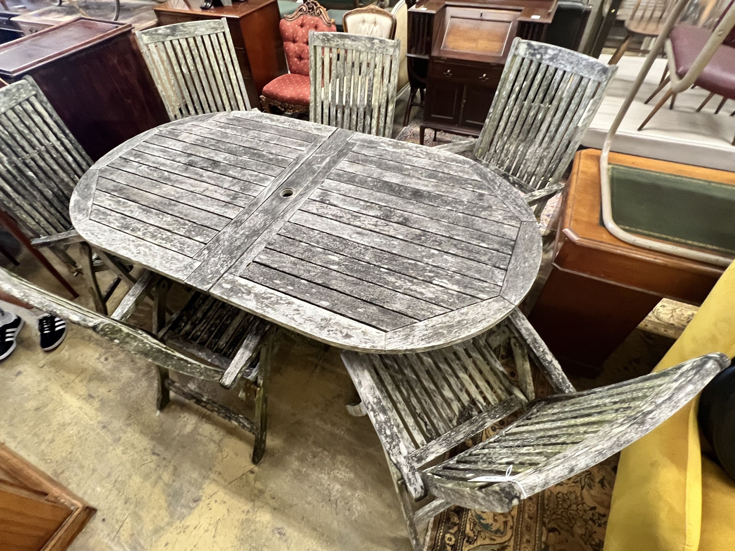 A weathered teak oval extending garden table, extended 250cm width 109cm height 73cm, and six folding garden elbow chairs